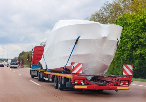 Truck semi-trailer carrier towing new wrapped yacht boat on highway road summer day. Delivering transportation new private Luxury ship. Rich recreation lifestyle. Service maintenance transportation.